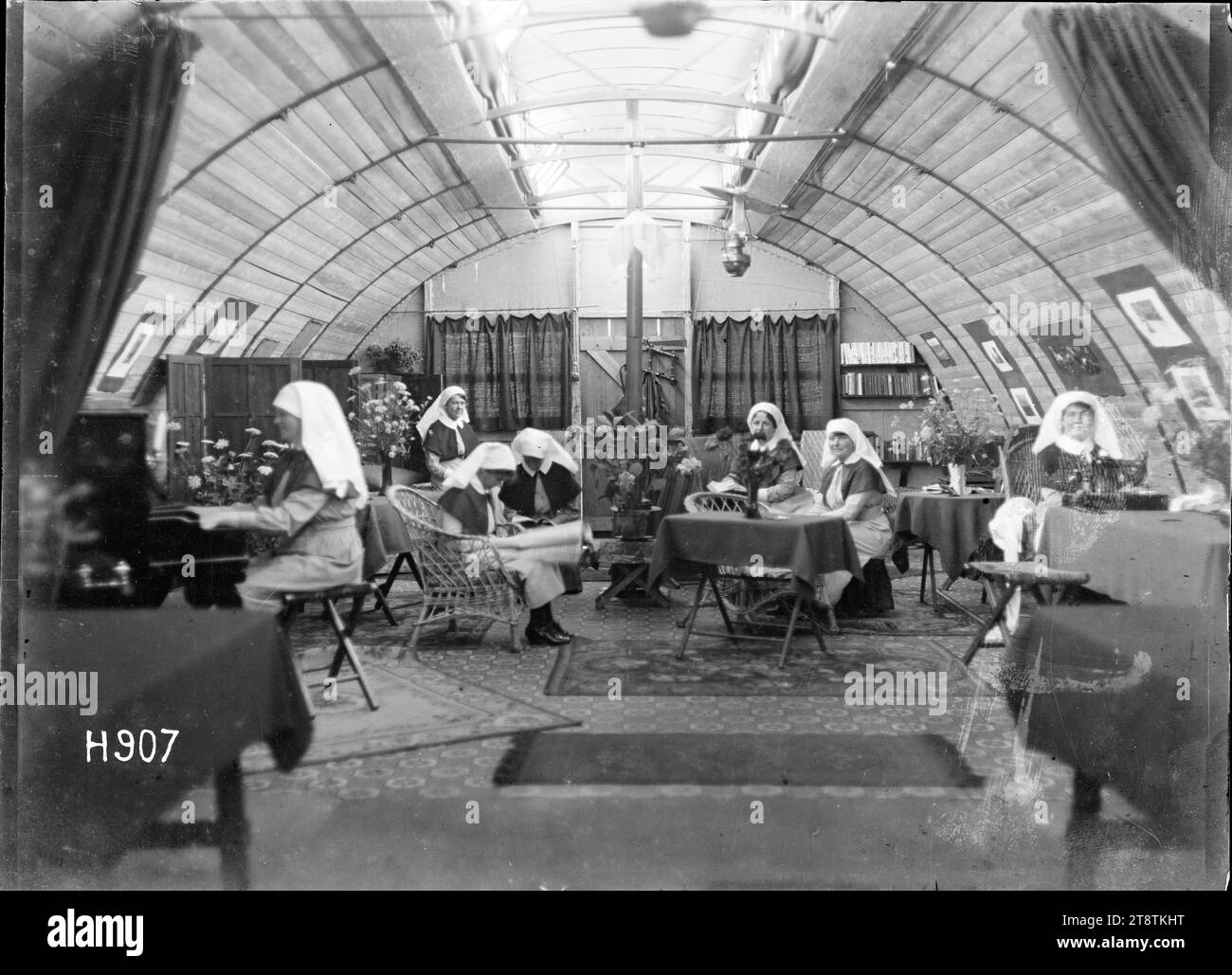 Im Inneren der Schwestern-Lounge im New Zealand Stationary Hospital in Wisques, Frankreich, im Inneren der Schwestern-Lounge und des Aufenthaltsraums im New Zealand Stationary Hospital in Wisques während des Ersten Weltkriegs Zeigt eine Schwester, die Klavier spielt, während andere sitzen und lesen. Das Zimmer ist mit Vorhängen, Korbstühlen und Tischen ausgestattet. Es gibt gemusterte Teppiche auf dem Boden. Foto vom 16. August 1918 Stockfoto