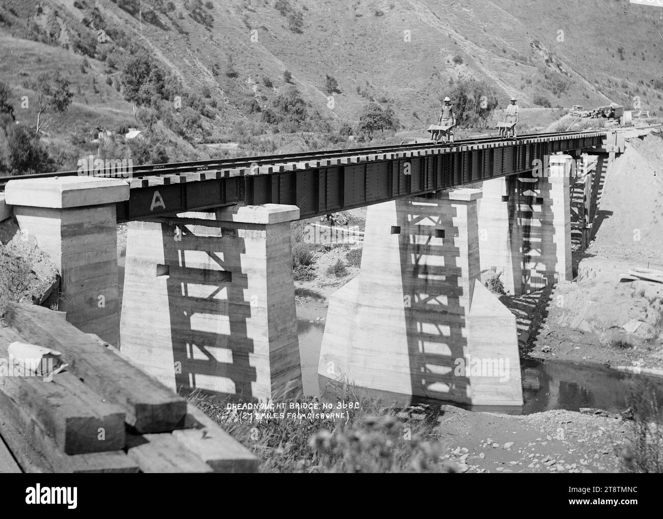 Dreadnought Eisenbahnbrücke, 43 km von Gisborne entfernt, Blick auf die neue Dreadnought Betonbahnbrücke, die über einen nicht identifizierten Fluss gebaut wurde, 27 km von Gisborne entfernt. Zwei Männer überqueren die Brücke und schieben Schubkarren voller Zementsäcke? Anfang der 1900er Jahre Stockfoto