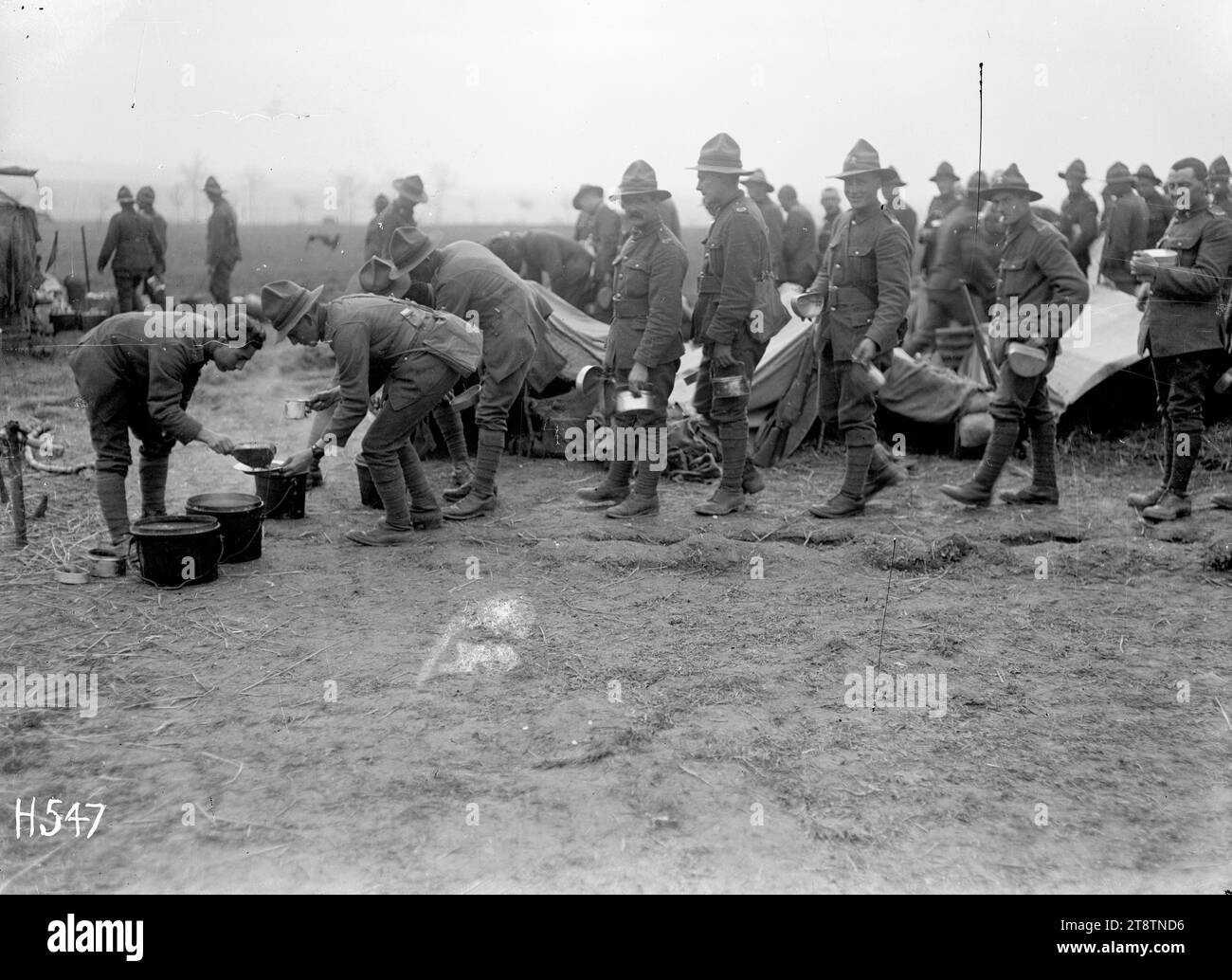 Mahlzeit für neuseeländische Truppen, Louvencourt, neuseeländische Soldaten, die sich mit ihren Schlangendosen für eine Mahlzeit im Lager in der Nähe von Louvencourt, Frankreich, während des Ersten Weltkriegs anstellen Ein Soldat schöpft Nahrung aus drei großen Töpfen. Foto vom 30. April 1918 Stockfoto