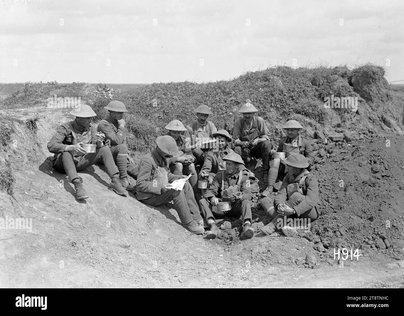 Ein neuseeländischer Soldat liest aus einer deutschen Zeitschrift, 1. Weltkrieg, neuseeländische Soldaten essen mittags eine Mahlzeit an der Front. Einer aus der Gruppe übersetzt aus einer deutschen Zeitschrift, die in einem Grabout gefunden wurde. Foto von Grevillers am 20. August 1918 Stockfoto