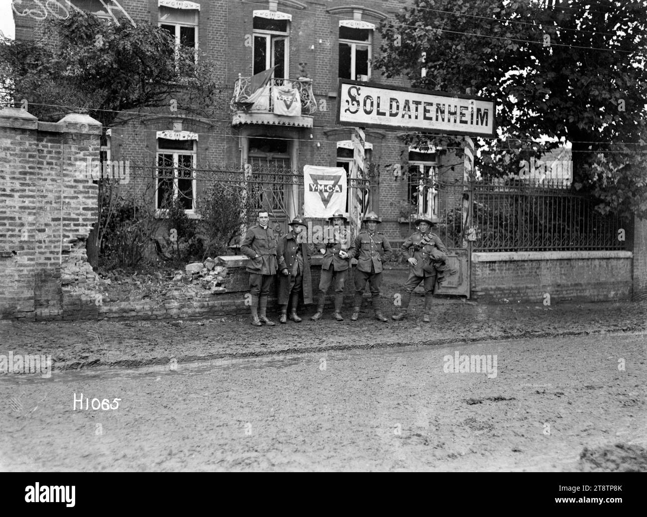 Soldaten außerhalb der neuseeländischen YMCA in Beauvois, Frankreich, 1. Weltkrieg, zeigt neuseeländische Soldaten, die während des Ersten Weltkriegs vor den neuseeländischen YMCA-Erholungsräumen in Beauvois, Frankreich warten Auf der Vorderseite des Gebäudes befindet sich ein Schild „Soldatenheim“, das darauf hinweist, dass es als Heim deutscher Soldaten genutzt wurde. YMCA-Banner und eine französische Trikolore-Flagge schmücken auch die Vorderseite, 14. Oktober 1918 Stockfoto