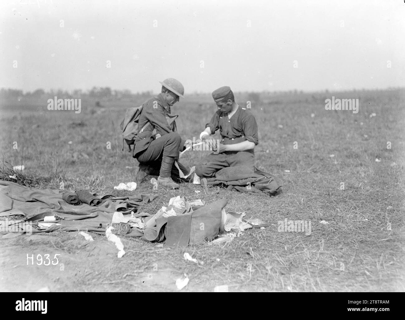 Ein neuseeländischer Soldat aus dem Ersten Weltkrieg verband einen deutschen Soldaten in Grevillers, Frankreich, Einen knienden neuseeländischen Soldaten, der den Arm eines leicht verwundeten deutschen Soldaten, der ebenfalls kniend ist, verband. Im Vordergrund sind Bandagen- und Verbandsrollen zu sehen. Foto aufgenommen am 24. August 1918 in Grevillers in Frankreich Stockfoto
