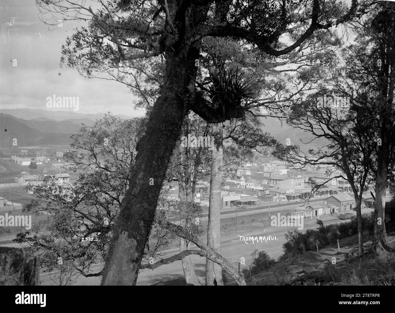 Allgemeiner Blick auf Taumarunui, Blick auf Taumarunui von Bäumen auf einem Hügel, mit dem Bahnhof im Zentrum im Vordergrund und der Hauptstraße hinter der Bahnlinie. Ca. 1910er Jahre Stockfoto