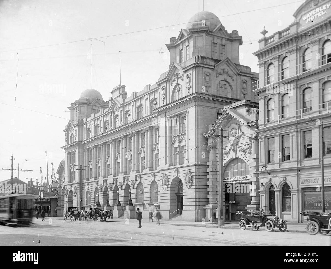 General Post Office und Queen Street Railway Station, Auckland, Neuseeland, Blick auf das neu errichtete General Post Office Gebäude. Auf der rechten Seite befindet sich der Eingang zum Bahnhof Queen Street und zum Waverley Hotel. Links vom Postgebäude befindet sich die R & W Hellaby Ltd (Metzgerei), weitere Stockwerke befinden sich im Bau über Hellabys Vor dem Postamt warten Pferdekutschen, und vor dem Hotel parkt ein Auto, ca. 1911-1912 Stockfoto