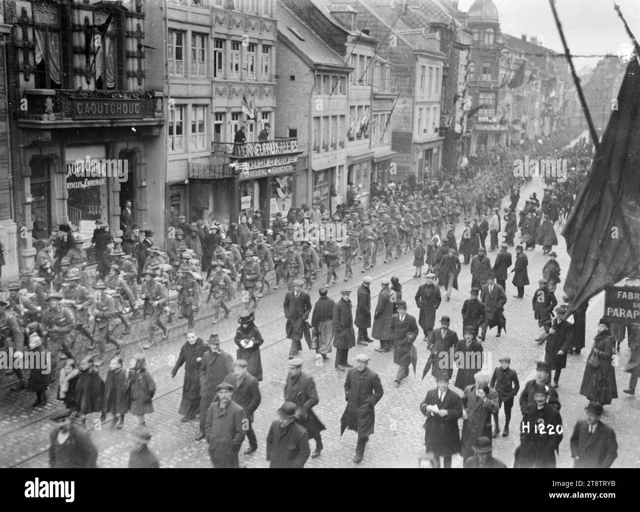 Neuseeländische Truppen marschieren nach dem Waffenstillstand durch eine Stadt in der Nähe des Rheins, Eine lange Kolonne neuseeländischer Truppen, die eine Kopfsteinpflasterstraße in einer Stadt (genaue Position unbekannt) entlang des Rheins nach dem Waffenstillstand, der den Ersten Weltkrieg beendete Eine Reihe von Flaggen fliegt von Gebäuden. Zivilisten auf der Straße sehen sich das Foto des Geschehens an, das Ende 1918 aufgenommen wurde Stockfoto