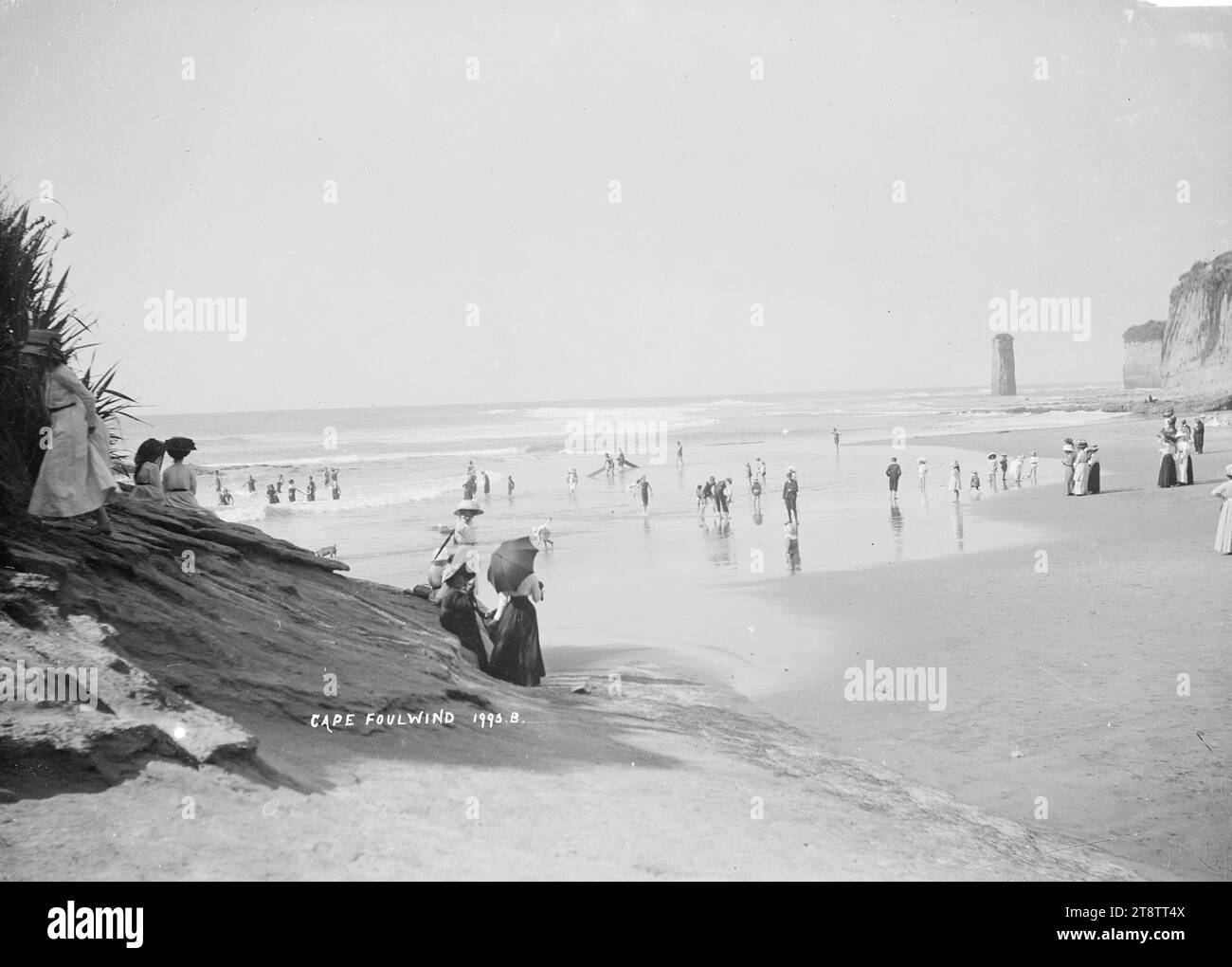 Cape Foulwind, Blick auf den Strand von Cape Foulwind. Zeigt eine große Anzahl von Menschen am Strand, eine Gruppe schwimmt, eine Reihe von Frauen mit Sonnenschirmen und eine Felssäule, die im Meer am anderen Ende des Strandes steht. Foto, aufgenommen um 1910 von William Price Stockfoto