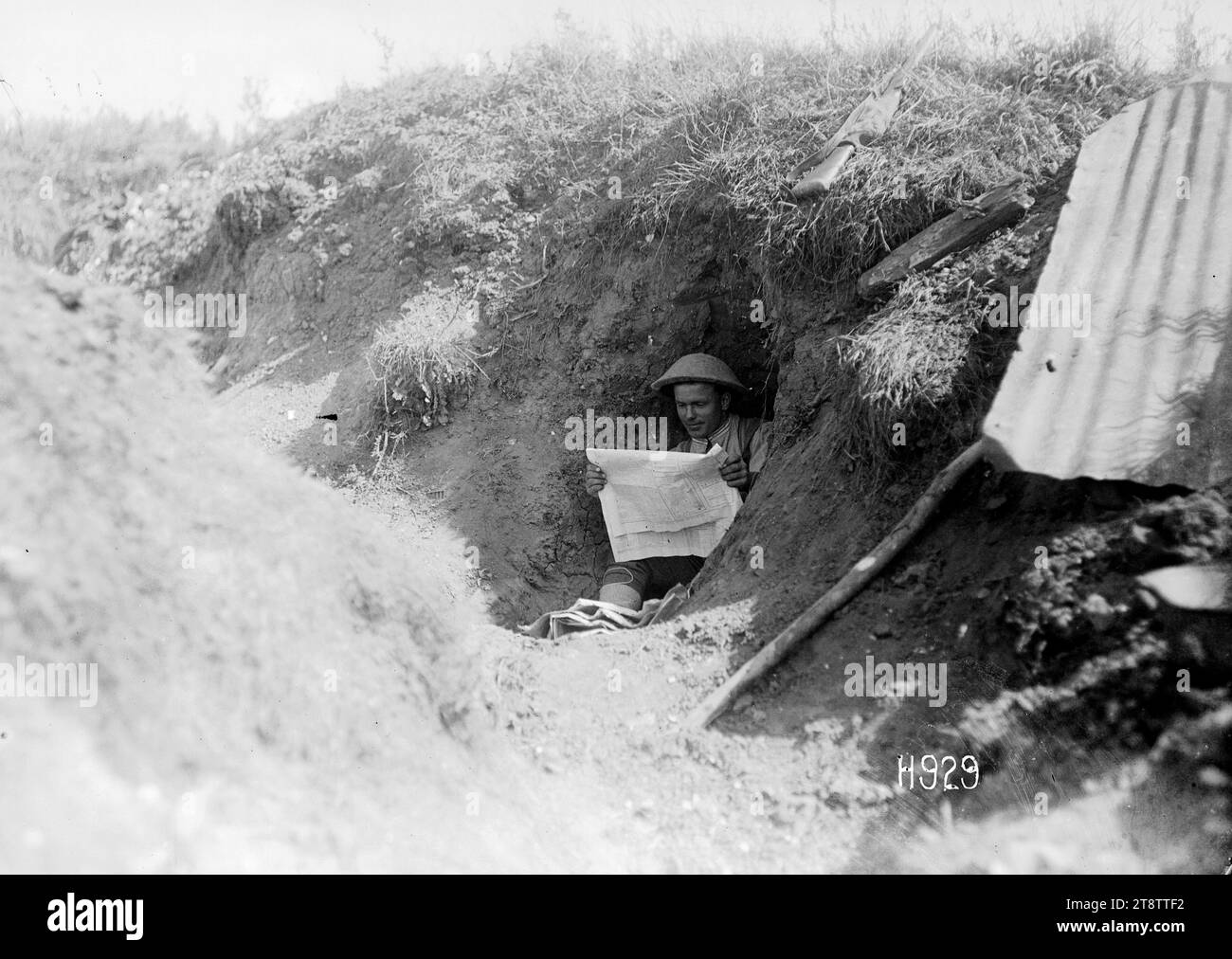 Ein neuseeländischer Soldat liest eine Zeitung in einem gefangengenommenen deutschen Graben, Frankreich, Ein neuseeländischer Soldat oder "Digger", der in einem Funk-Loch eines Grabens sitzt, der vor kurzem von den Deutschen gefangen genommen wurde. Der Soldat liest eine neuseeländische Zeitung. Ein Gewehr liegt auf dem Gras darüber. Foto: Puisieux am 21. August 1918 Stockfoto