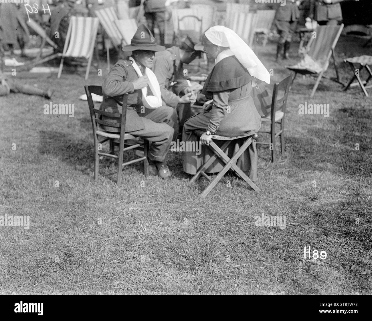 Ein verwundeter Soldat aus dem Ersten Weltkrieg spricht mit einer Krankenschwester auf der Gartenparty auf dem Gelände des New Zealand Stationary Hospital, Ein sitzender verwundeter neuseeländischer Soldat spricht mit einer Krankenschwester auf der Gartenparty auf dem Gelände des New Zealand Stationary Hospital, wahrscheinlich in Hazebrouck. Frankreich, während des Ersten Weltkriegs Foto vom 24. Juni 1917 Stockfoto