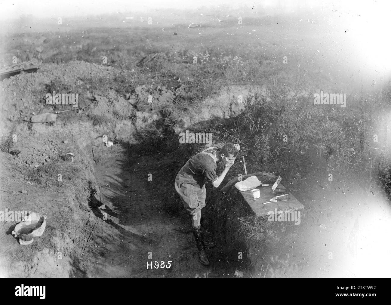 Brigadegeneral Herbert Hart steht in Hemden und rasiert sich im Ersten Weltkrieg außerhalb seines Einstiegs in der Nähe von Bapaume Zeigt einen Becher, einen gerissenen Spiegel, eine Zahnbürste und eine Haarbürste auf einer Holzplatte. Der Brigademeister beugt sich, um in den Spiegel zu schauen. An seiner weggeworfenen Jacke steckt ein Bajonett in der Bank. Foto, aufgenommen Ende August 1918 Stockfoto