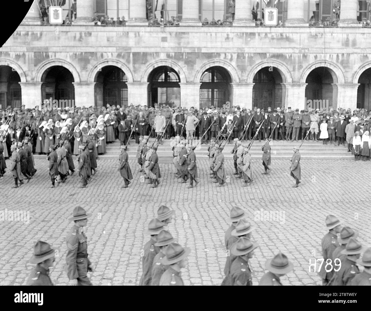 Französische Truppen marschieren am Fete National, Hazebrouck, Ein allgemeiner Blick über den Stadtplatz, von den französischen Truppen, die bei den offiziellen Feierlichkeiten für das Fete National, Hazebrouck, vorbeimarschieren. Beamte und Gäste stehen auf den Stufen des Rathauses? Links stehen Schwestern aus dem stationären Krankenhaus NZ. Im Vordergrund marschieren neuseeländische Soldaten. Foto vom 14. Juli 1917 Stockfoto