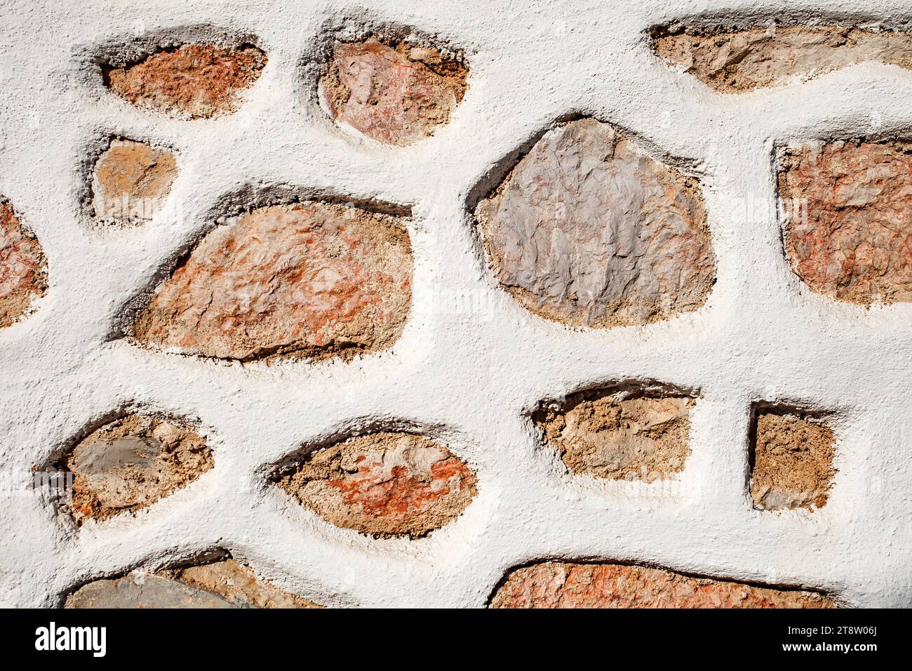 Wand aus roten und grauen verschiedenen Steinen Hintergrund, Textur unregelmäßige Formen, Steinzaun mit weißem Kitt. Stockfoto