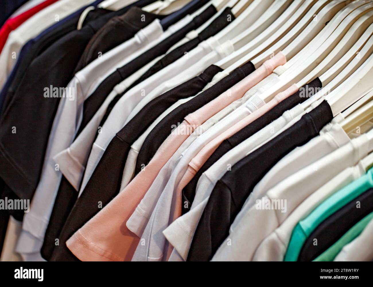 Kleidung aus mehrfarbigen Stoffen und Textilien, die in einem Bekleidungsgeschäft an Kleiderbügeln hängen Stockfoto