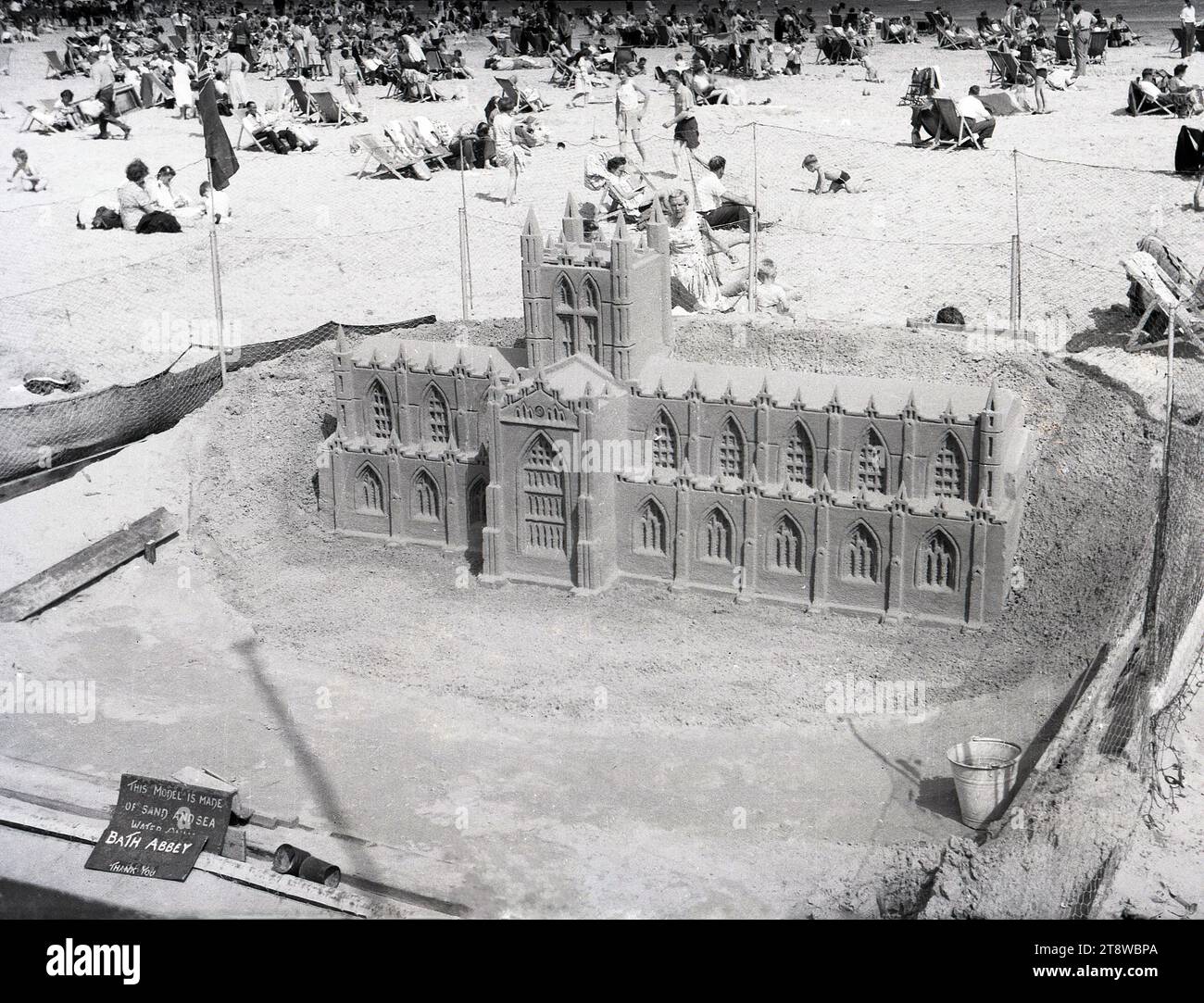 1950er Jahre, historisch, am Strand, Menschen auf Liegestühlen und ein Sandmodell von Bath Abbey, England, Großbritannien. Die Überschrift besagt: „Dieses Modell besteht nur aus Sand und Meerwasser“. Die 1611 eröffnete Bath Abbey in Somerset, offiziell bekannt als Abteikirche St. Peter und St. Paul, ist ein im gotischen Stil erbautes Benediktinerkloster. Stockfoto