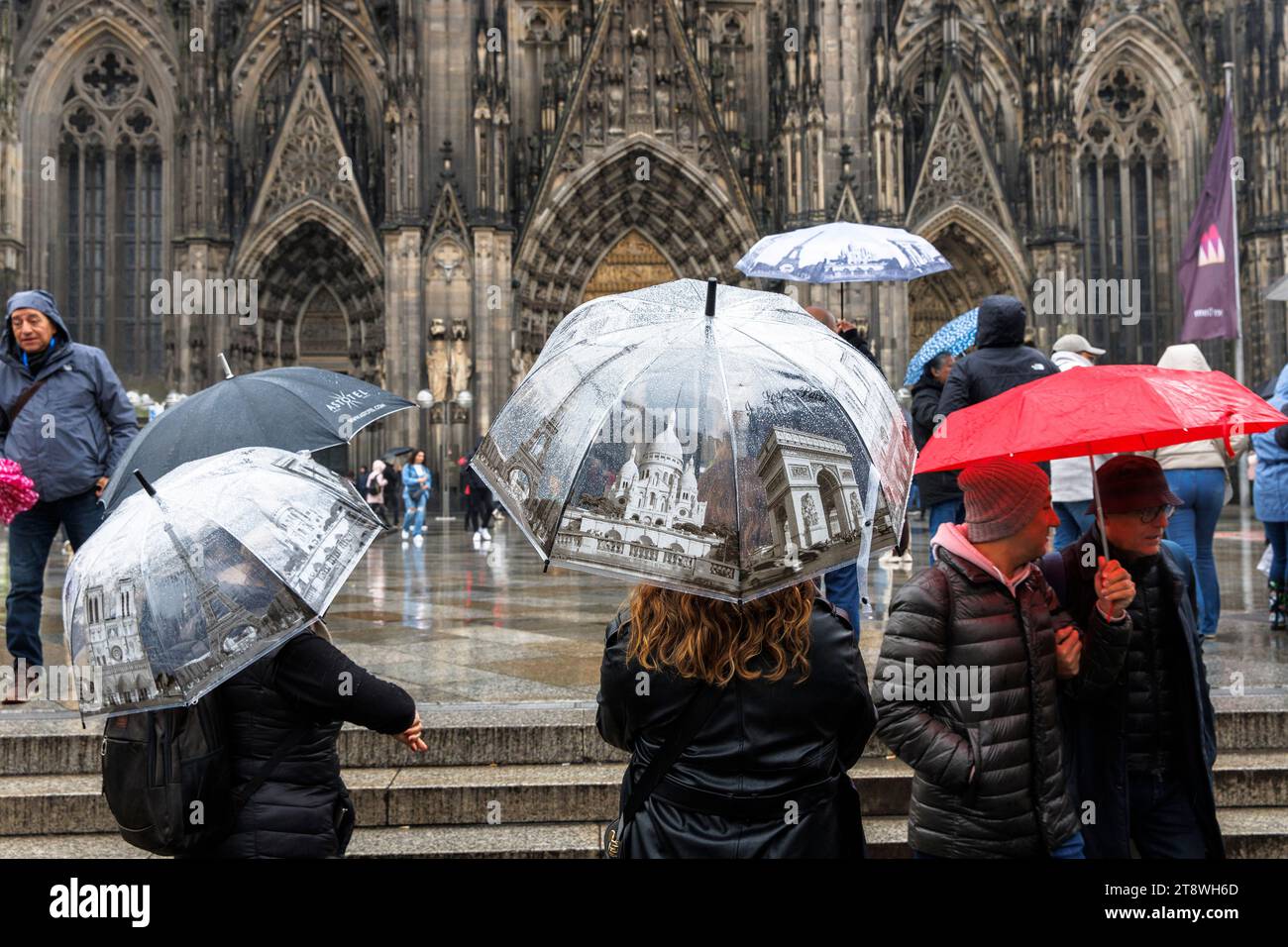 Touristen mit Sonnenschirmen im Pariser Stil vor dem Dom, Köln, Deutschland. Touristen mit Regenschirmen mit Paris Motiven stehen bei Regen vor d Stockfoto