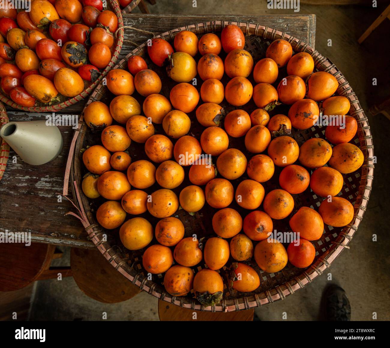 Reife orangefarbene Persimmonen. Auf dem Tisch auf dem Markt. Ein Haufen Bio-Persimmon-Früchte auf einem lokalen Bauernmarkt in Dalat, Vietnam. Persimmon BA Stockfoto
