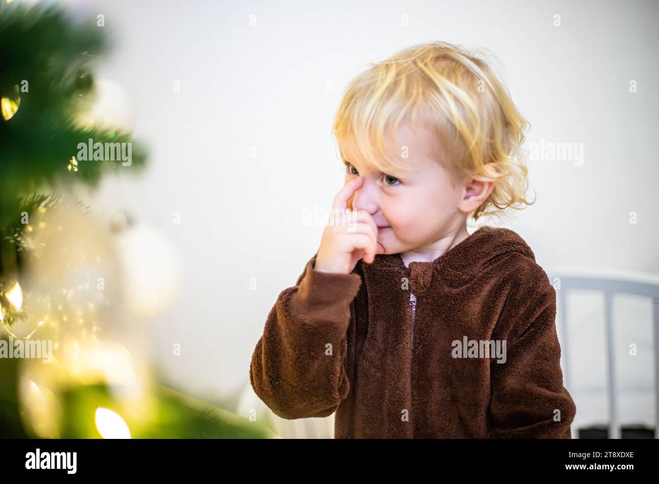 Ein kleines Mädchen in einem Karnevalskostüm denkt darüber nach, mit welchem Spielzeug man einen Weihnachtsbaum dekorieren soll Stockfoto