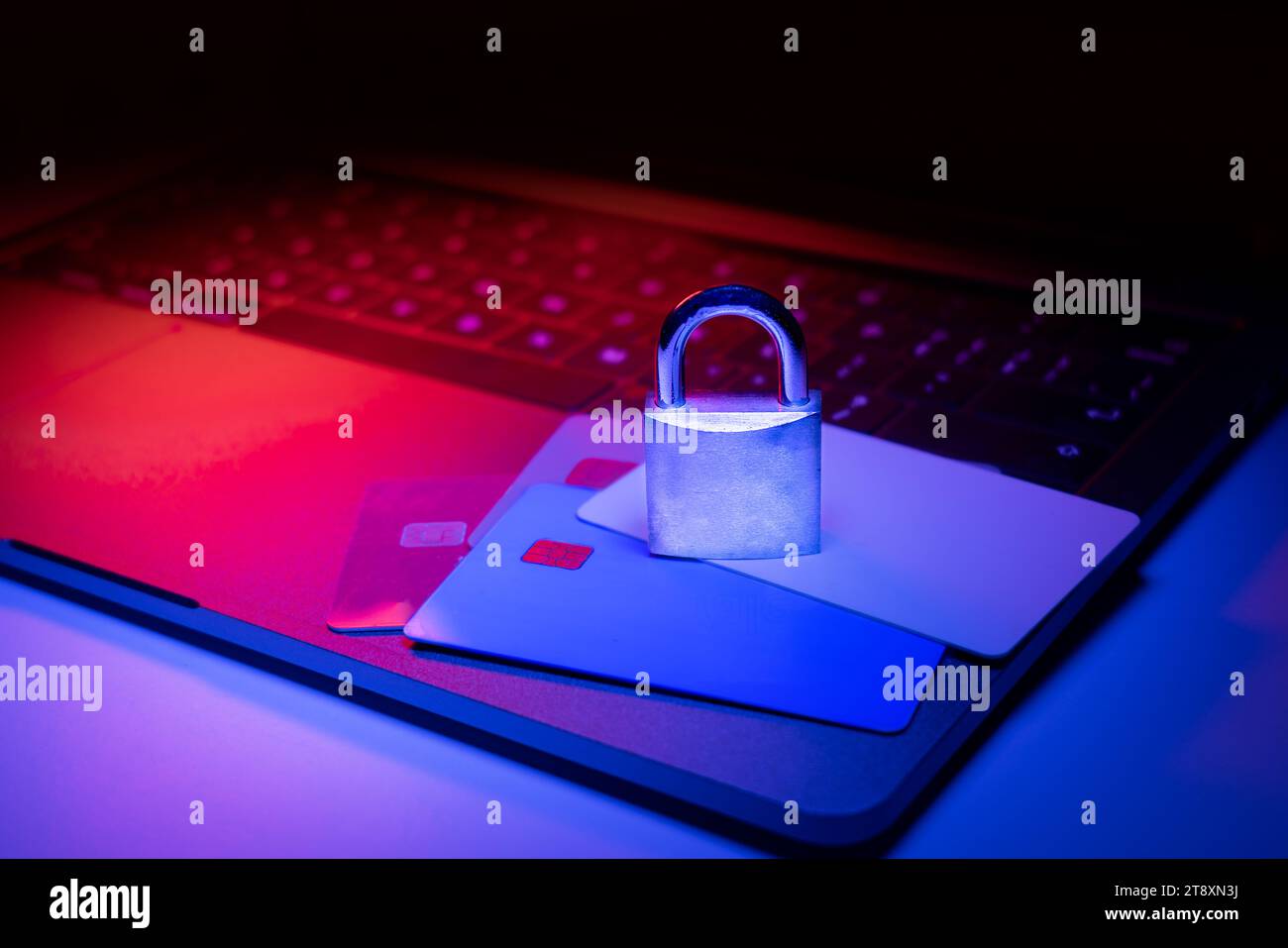 Großaufnahme eines Vorhängeschlosses auf einem Laptop und einer Kreditkarte, die mit blauem und rotem Licht beleuchtet ist. Phishing, Cybersicherheitsgefahr oder Ransomware-Angriff. Verschlüsselte p Stockfoto