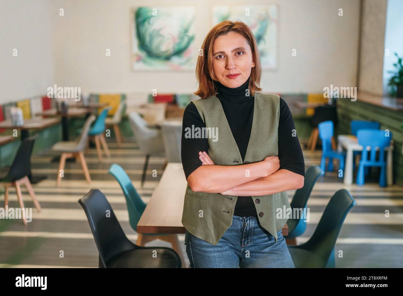 Porträt einer lächelnden kleinen Geschäftsfrau, die in Küchenuniform in ihrem gemütlichen Restaurantsaal gekleidet ist. Erfolgreiche Menschen, harte Arbeit, Verbraucher, Café Stockfoto