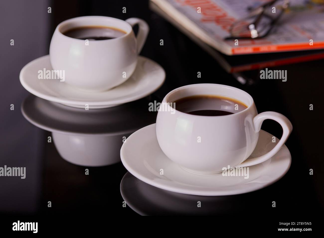Tassen Kaffee in weißen Tassen und Untertassen mit einem Magazin im Hintergrund. Stockfoto