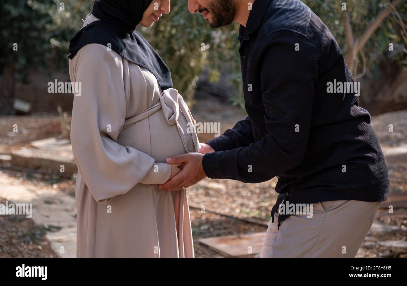 Ein Ehemann spaziert mit seiner schwangeren Frau im Park, tauscht liebevolle Blicke aus und fühlt sich aufgeregt über die bevorstehende Geburt Stockfoto