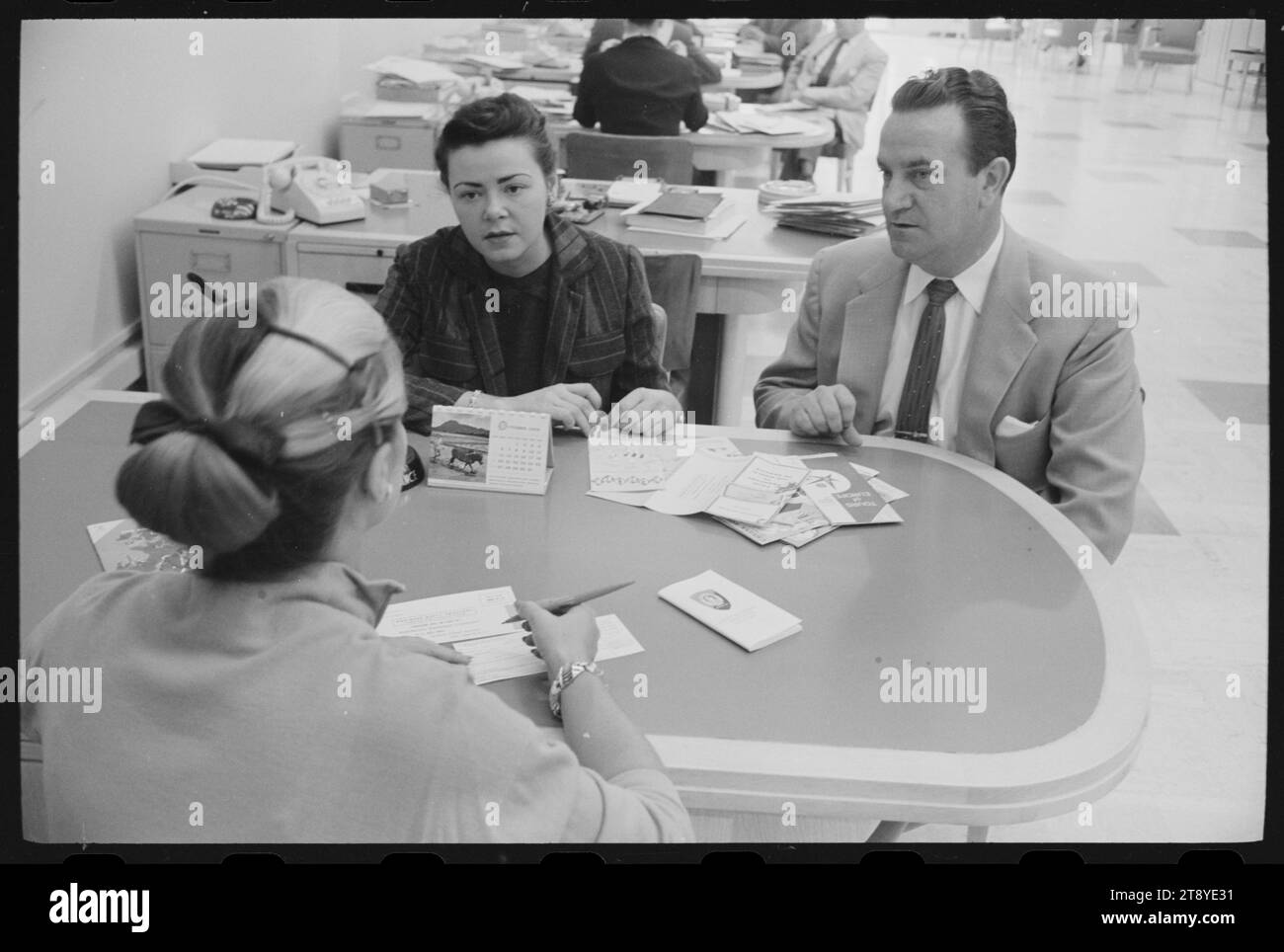 Ein Paar sieht sich Reisebroschüren an, während er eine Kreditkarte im American Express Büro in Washington, District of Columbia, 10.08.1958, beantragt. Foto: Thomas O'Halloran/US News and World Report Magazine Collection Stockfoto