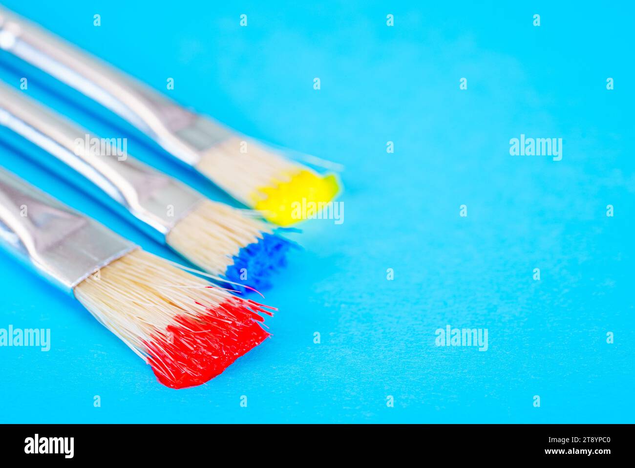 Pinsel mit roter, blauer und gelber Farbe auf blauem Hintergrund Stockfoto