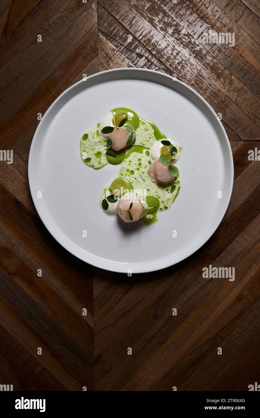 Jakobsmuscheln auf einem großen runden weißen Teller auf einem Holztisch, das Gericht eines großartigen Küchenchefs. Stockfoto