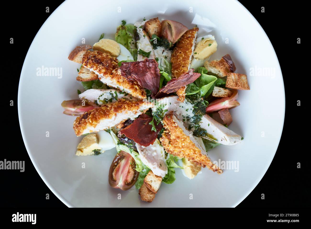 Präsentation von Chicken Caesar Salat auf einem runden weißen Teller, Draufsicht, schwarzer Hintergrund Stockfoto