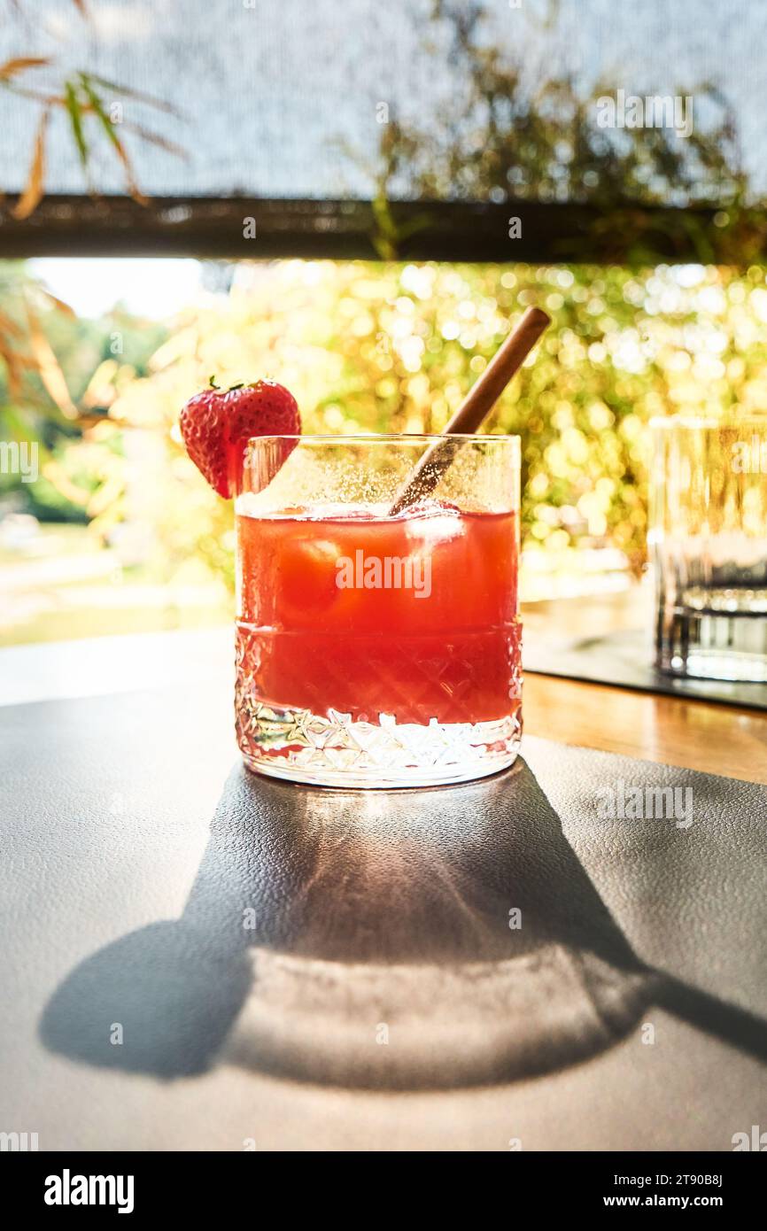 Ein Seitenblick auf einen roten Fruchtcocktail mit Eis und Stroh auf einem Holztisch in der Sommersonne. Stockfoto