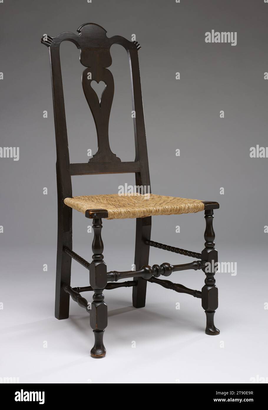 East Windsor Side Chair, 1770–90, zugeschrieben Timothy Loomis III, amerikanisch, 1724–1786, 41 5/8 x 19 1/4 x 15 1/2 cm. (Ca. 105,73 x 48,9 x 39,37 cm), Kirsche, Asche, Pigment, Pflanzenfasern, USA, 18. Jahrhundert, dieser Stuhl besticht durch seine unverwechselbare Dekoration. Der vasenförmige Splat oder der mittlere hintere Abschnitt hat ein ausgeschnittenes Herz. Die gewellte obere Schiene ist in der Mitte mit einem „Pagode“-Design und auf jeder Seite mit geschnitzten „Ohren“ versehen. Die flachen, geschnitzten Stützfüße und die geschwungene hintere Schiene sind die Details eines ambitionierten Handwerkers, eines Tischlers der dritten Generation aus dem Connecticut River Valley Stockfoto