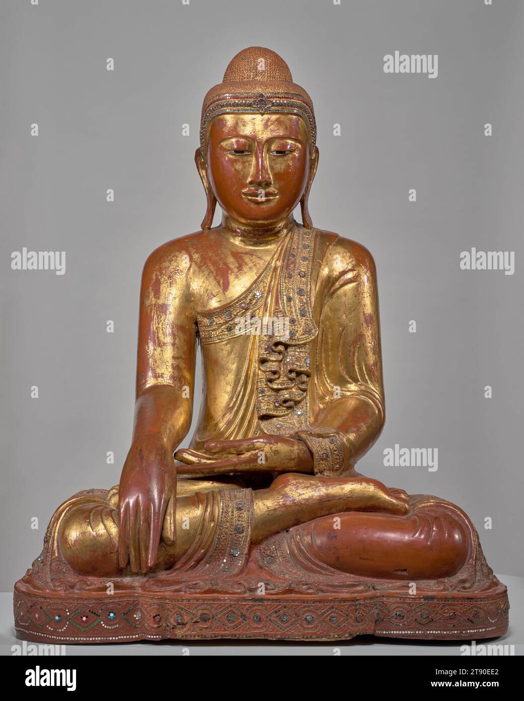 Verankerter Buddha, ca. 1850, 41 1/2 x 32 x 23 Zoll (105,41 x 81,28 x 58,42 cm), Holz, Lack, Blattgold, Spiegel und farbige Glasintarsien, Myanmar (Burma), Mandalay-Stil, im bhumisparśamudra sitzend, oder erdberührende Geste, zeigt diese Statue den Buddha kurz vor seiner Erleuchtung unter dem Bodhi-Baum. Die Ereignisse, die bis zu diesem Moment geführt haben, werden oft als ein mächtiger Kampf zwischen gut und Böse, Wahnvorstellungen und Einsichten beschrieben. Mara, der Gott der Illusion, Griff Buddha an und forderte das Recht des jungen Prinzen auf, ihn zu zerstören. Als Reaktion darauf erreichte der Buddha seine rechte Hand nach unten Stockfoto