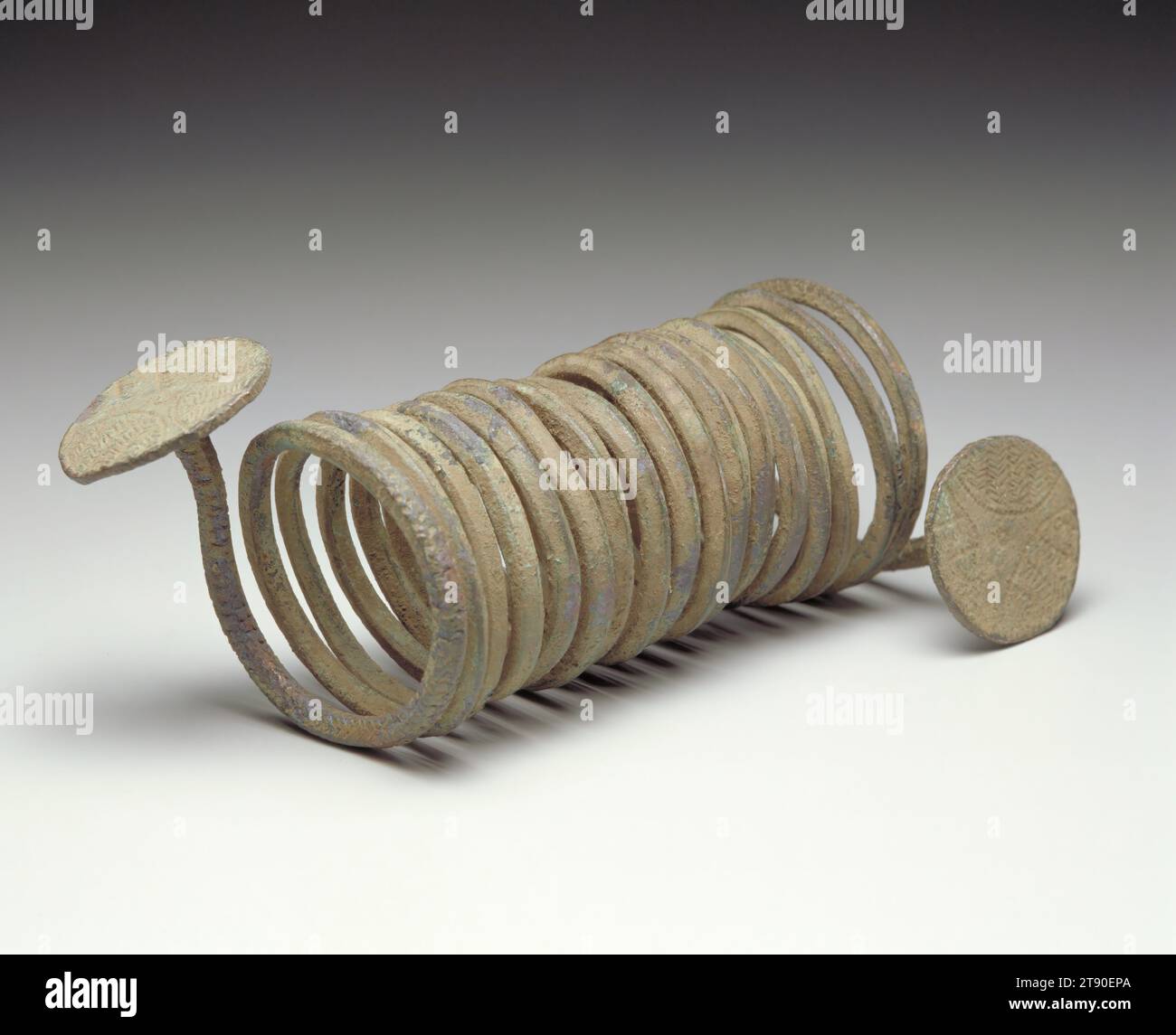 Währung, 20. Jahrhundert, 11 x 5 1/4 x 3/8 Zoll (27,94 x 13,34 x 8,57 cm), Kupfer, Nigeria, 20. Jahrhundert, in den späten 1400er Jahren begannen die Portugiesen mit Igbo-Völkern im Südosten Nigerias zu handeln, wobei sie zunächst hauptsächlich Elfenbein und Pfeffer kauften, später auch Menschen. Die Portugiesen tauschten für Waren mit Kupfer, die der Igbo im Laufe der Jahrhunderte anhäufte und verwandelte. Die so genannte Armbandwährung, die hier zu sehen ist, ist ein Erbe dieser Tradition. 17 Spulen bilden eine Metallfeder, die an ihren Enden flache Kreise hat. Einige Igbo-Währungen haben mehr oder weniger Coils, die den Betrag variieren Stockfoto