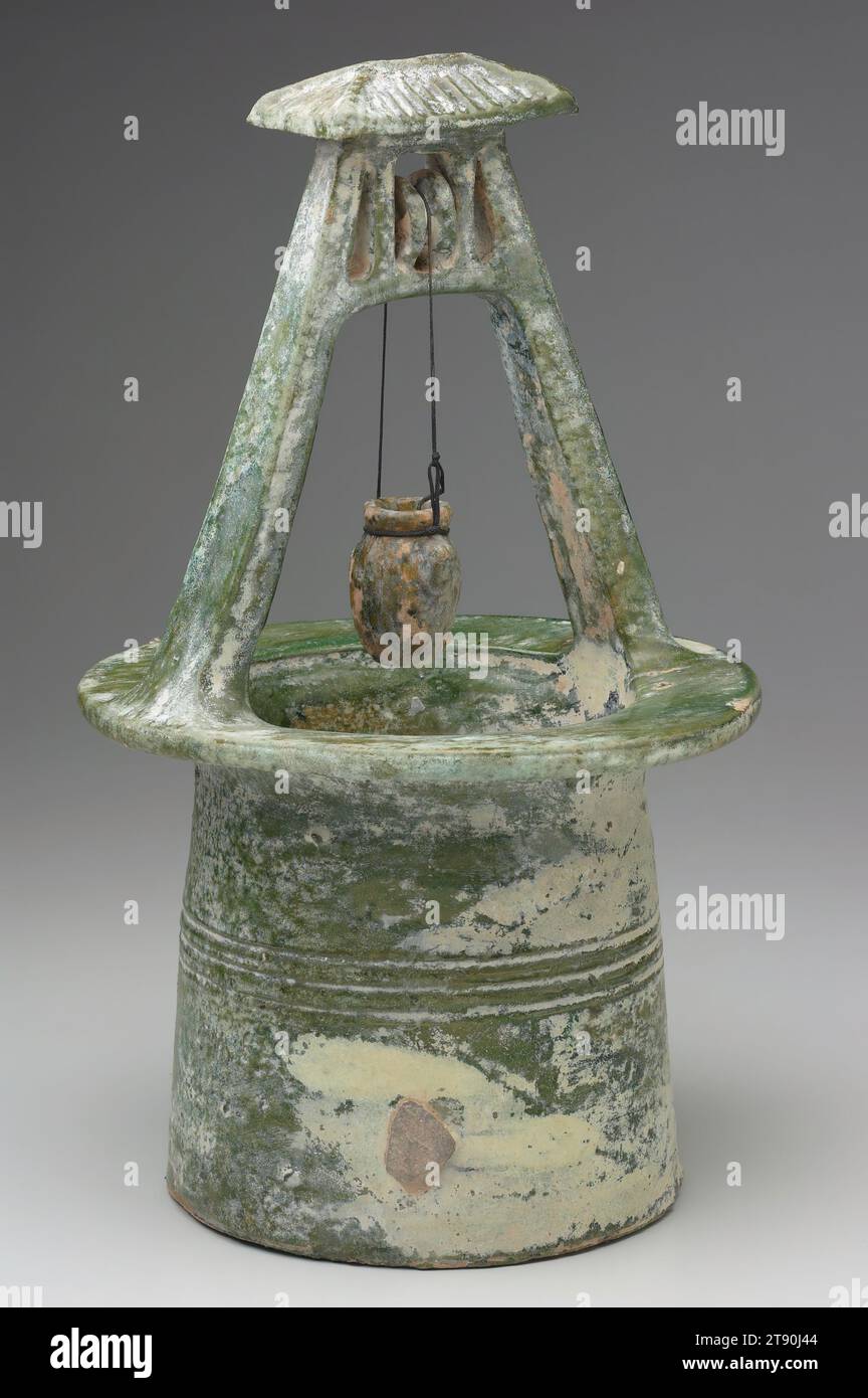 Bohrlochkopf, 1.-2. Jahrhundert, 15 3/4 x 8 3/4 Zoll (40 x 22,23 cm), niedrig befeuerter Steingut mit grüner Glasur, China, 1.-2. Jahrhundert. Dieser zylindrische Bohrlochkopf hat einen A-Rahmen-Aufbau mit einem quadratischen gerahmten Gehäuse für eine Riemenscheibe, das von einem gekachelten Hüftdach bedeckt ist. Ein Wassereimer zum Absenken in den Brunnen mithilfe der Seilrolle und des Seils rundet die Gruppe ab. Fast alles notwendige wurde in Han-Grabmöbeln bereitgestellt. In diesem Fall war ein Brunnen die Wasserquelle für das Jenseits Stockfoto