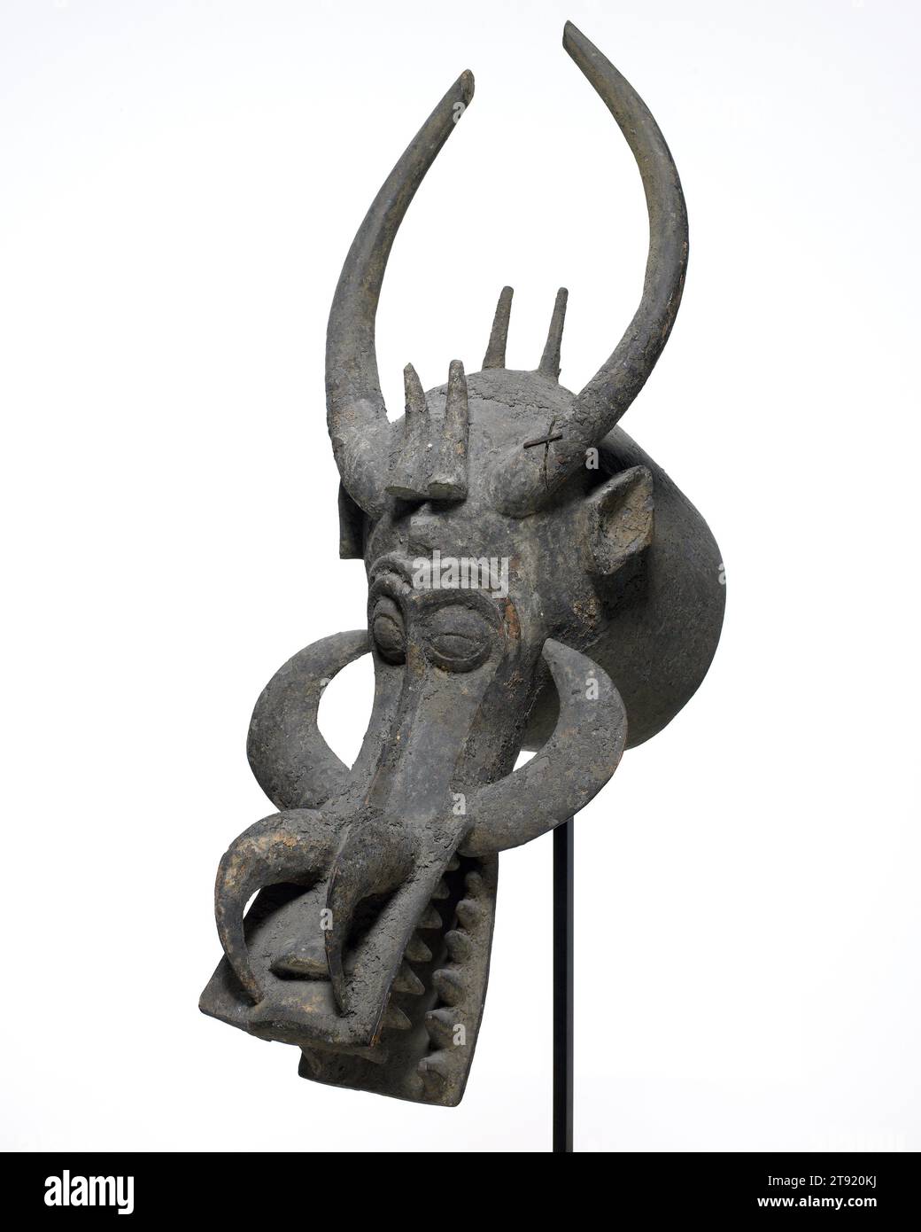 Maske, erste Hälfte des 20. Jahrhunderts, 30 1/2 x 11 1/4 x 20 1/2 Zoll (77,47 x 28,58 x 52,07 cm), Holz, Pigment, Metall, Côte d'Ivoire, 20. Jahrhundert, diese Maske ist ein "Feueropfer". Der Träger legt getrocknete Gräser und glühende Holzspäne in den Mund und bläst darauf, normalerweise bei nächtlichen Aufführungen, wenn der Effekt am dramatischsten ist. Wenn Sie näher an die Maske herankommen, sehen Sie eine Reihe von fressenden Kiefern, dolchartigen Stoßzähnen und mehreren Hörnern. Die Maske soll den Schrecken der Zauberei hervorrufen und gleichzeitig die Art von übernatürlichem Krieg vermitteln, die nötig ist, um die Gemeinschaft zu schützen Stockfoto