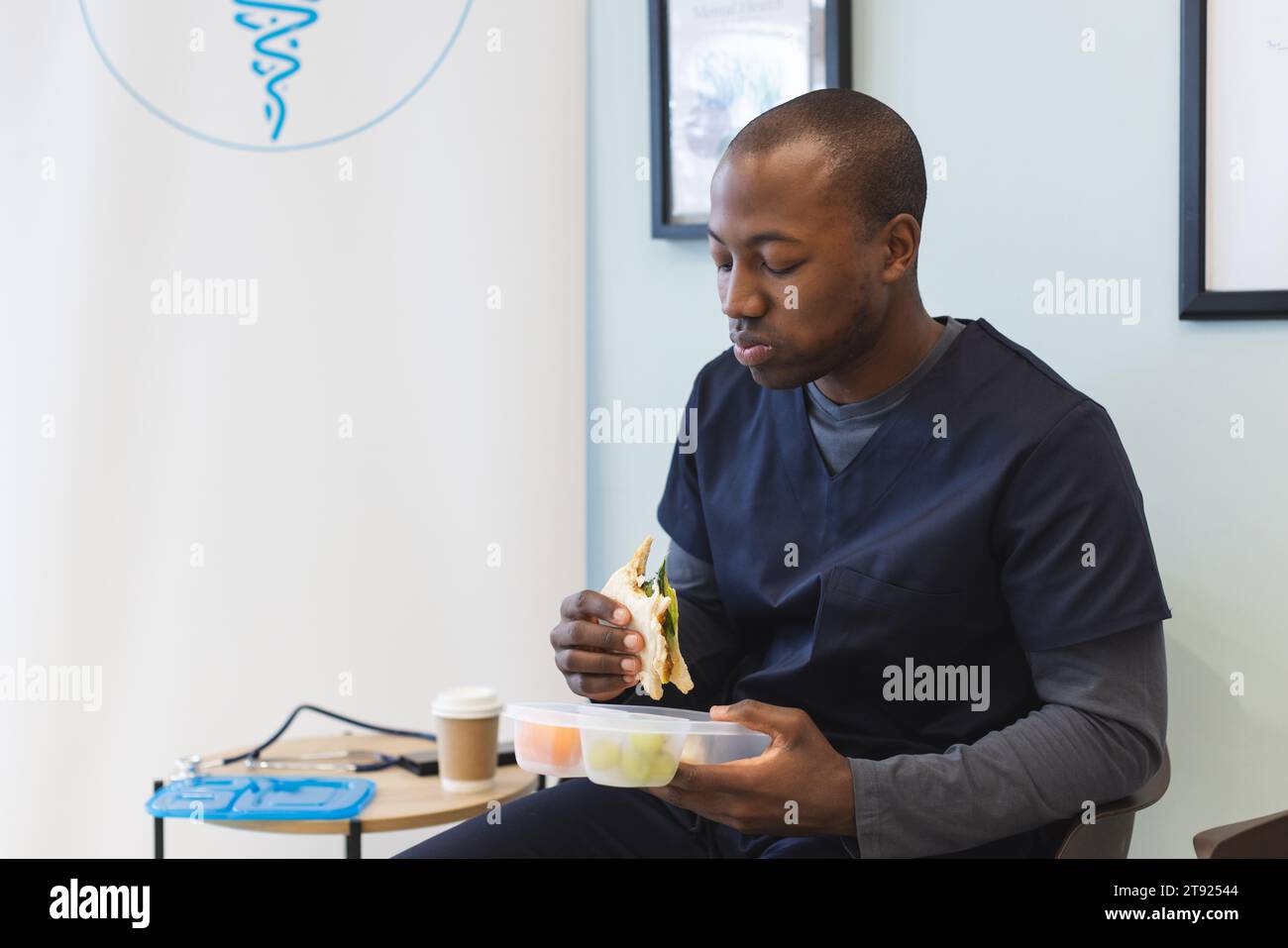 afroamerikanischer männlicher Arzt, der im Wartezimmer im Krankenhaus Peelings trägt, essen Essen zum Mitnehmen Stockfoto