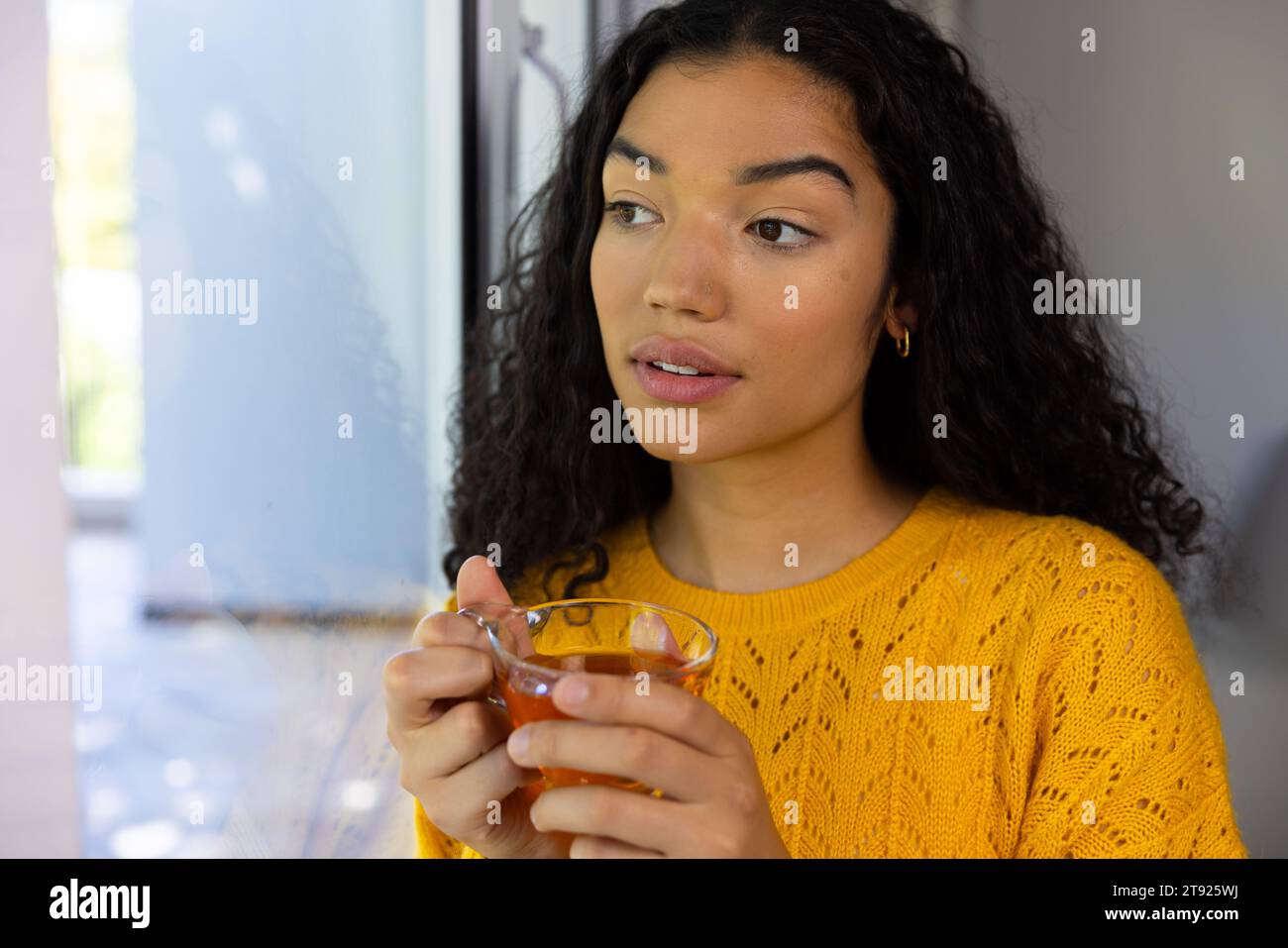 Birassische Frau, die eine Tasse Tee hält und zu Hause aus dem Fenster blickt Stockfoto