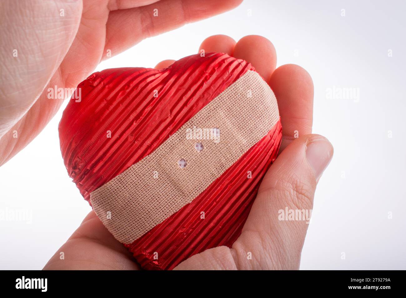Hand, die ein verletztes Herz mit Gips in der Hand auf weißem Hintergrund hält Stockfoto