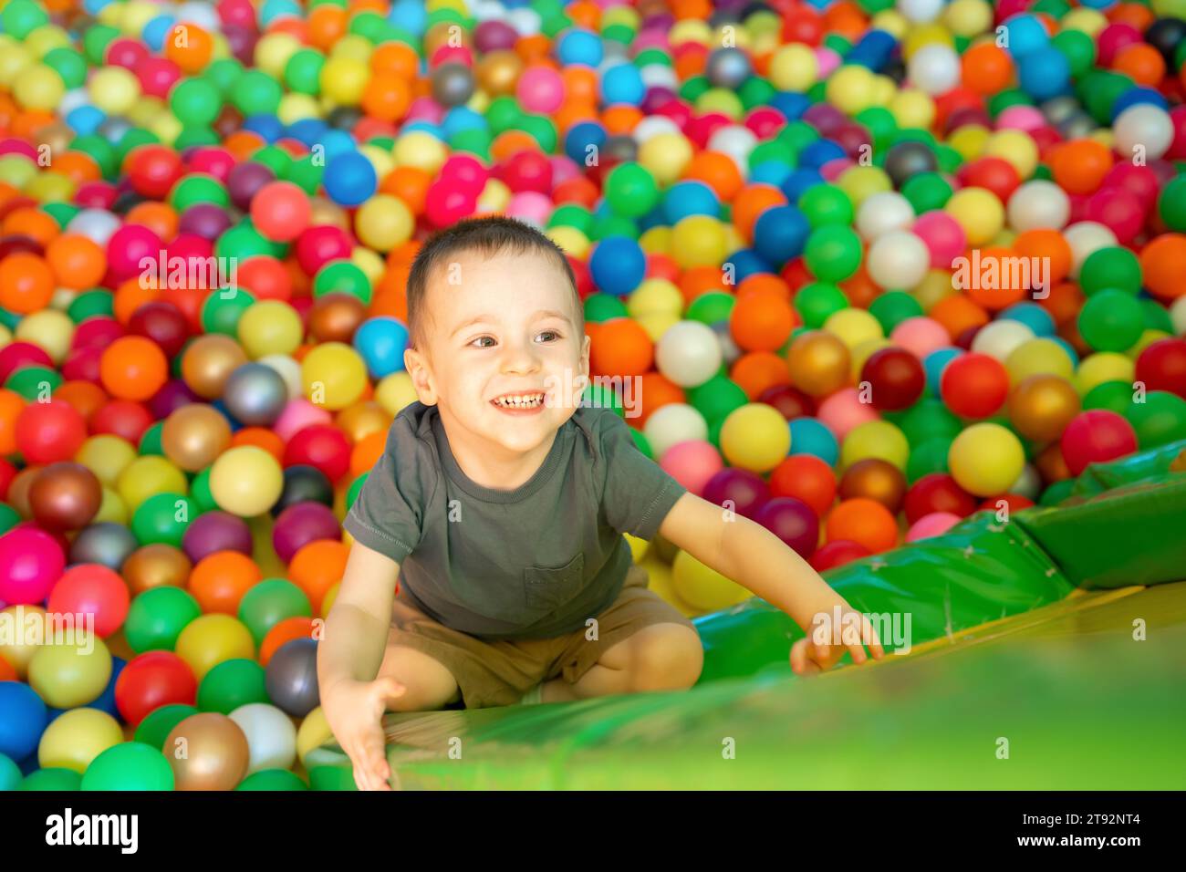 Fröhlich lächelnder kleiner Junge klettert auf einer Rutsche in einem Kinderzimmer oder im Kinderunterhaltungs-Center. Mehrfarbige Kugeln. Fröhliche aktive Freizeit und Stockfoto