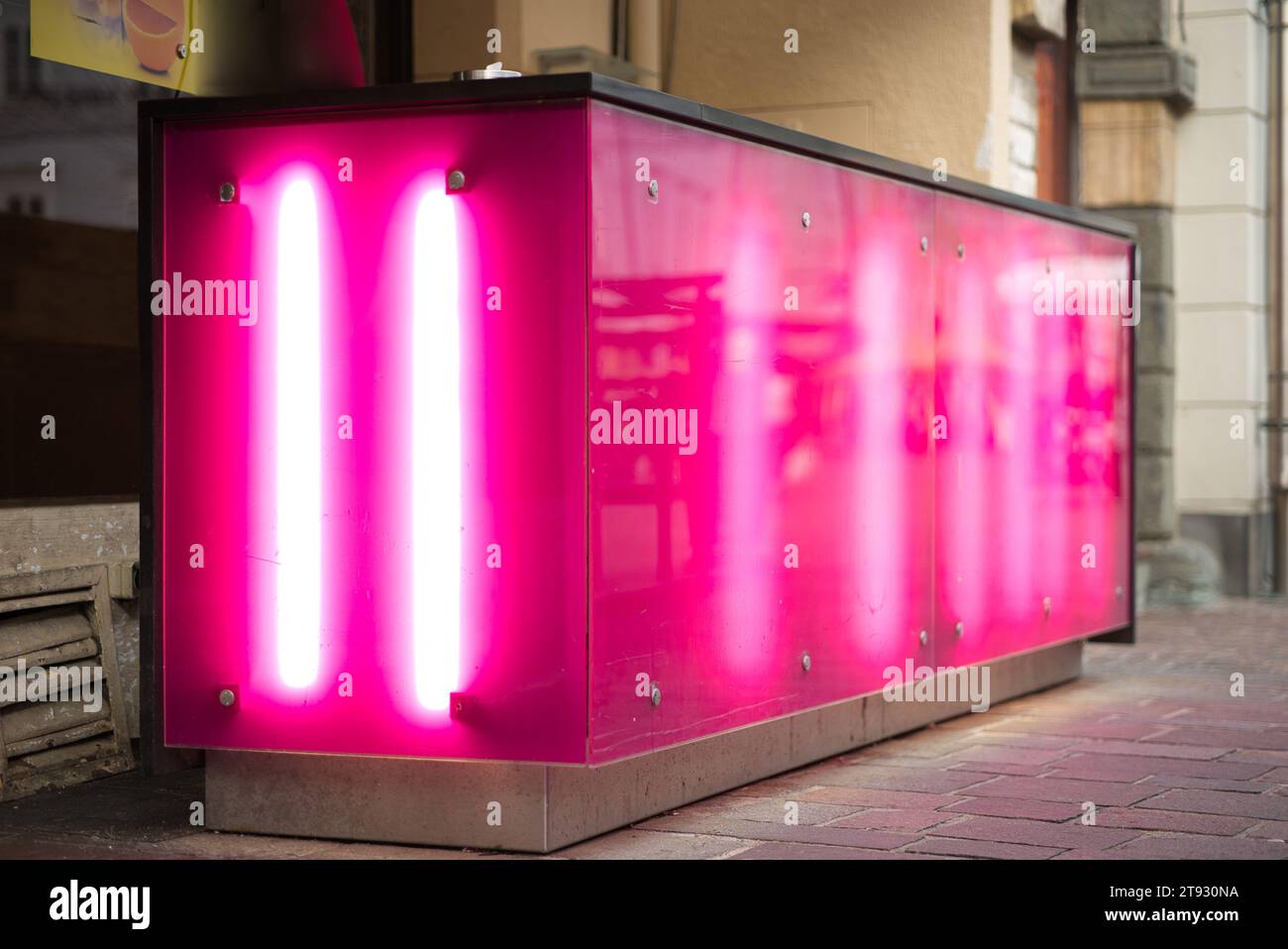 Erkunden Sie das lebhafte Ambiente einer Bar im Freien mit rosa hintergrundbeleuchteten Fassaden, die von Neonröhren beleuchtet werden. Im Freien eines Fußgängerzos gelegen Stockfoto