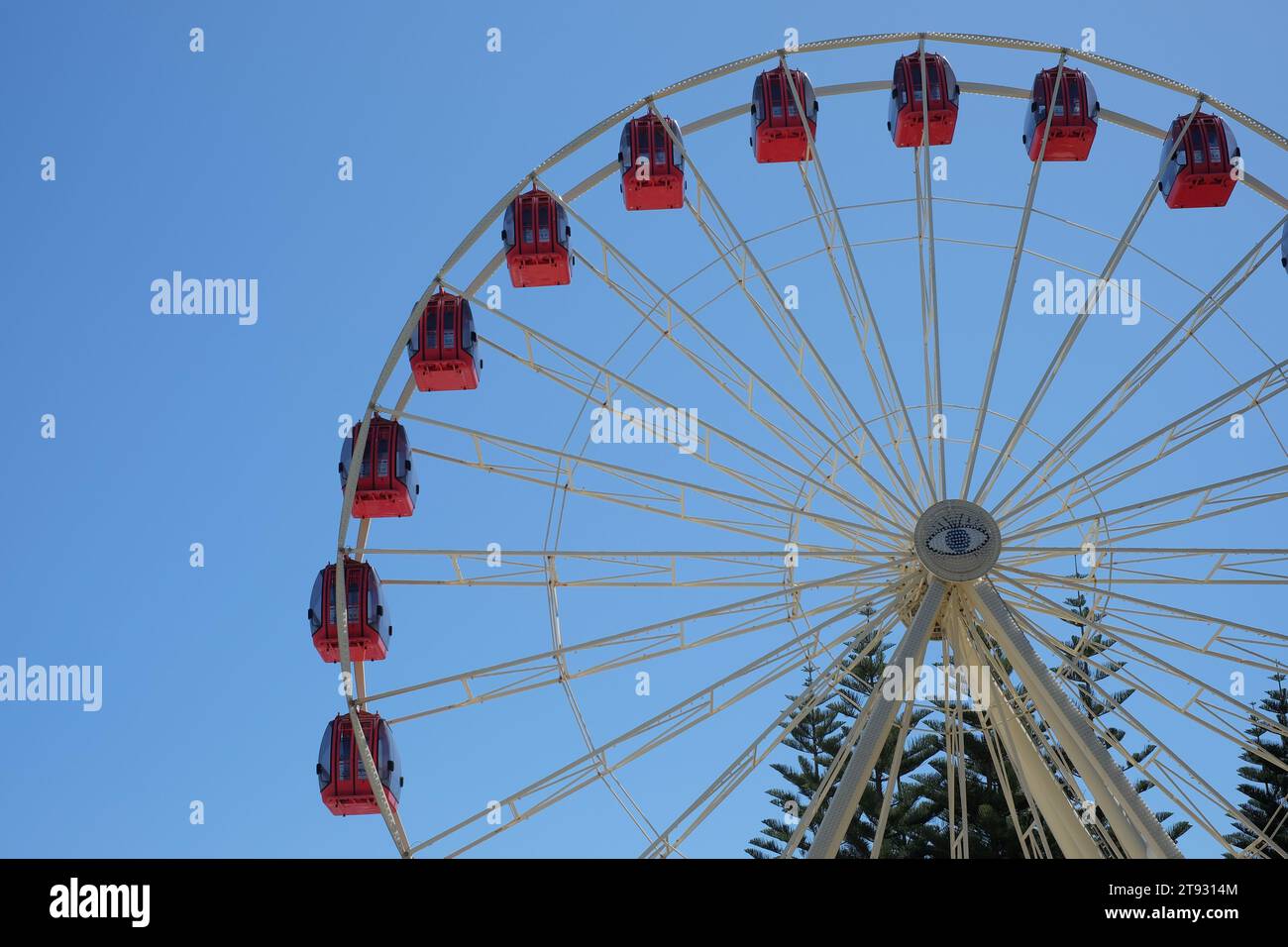 Rote Gondeln säumen den Umfang des Tourist Wheel Fremantle, eine beliebte Attraktion des Riesenrades, mit einem zentralen Augenmotiv vor einem blauen Himmel Stockfoto