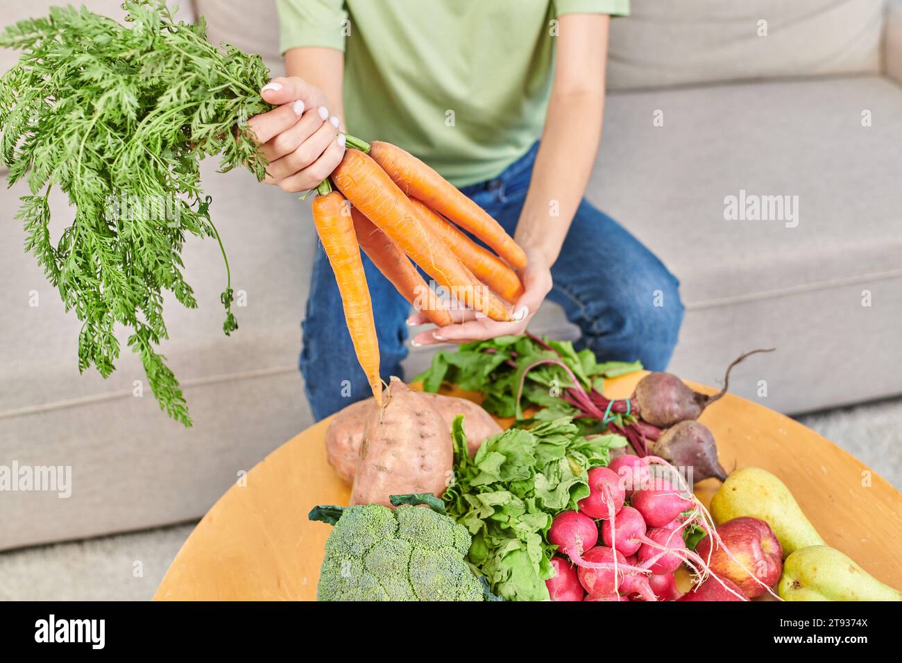 Zugeschnittene Ansicht einer Frau, die frische Karotten über verschiedenen Gemüse und Früchten hält, pflanzliche Ernährung Stockfoto