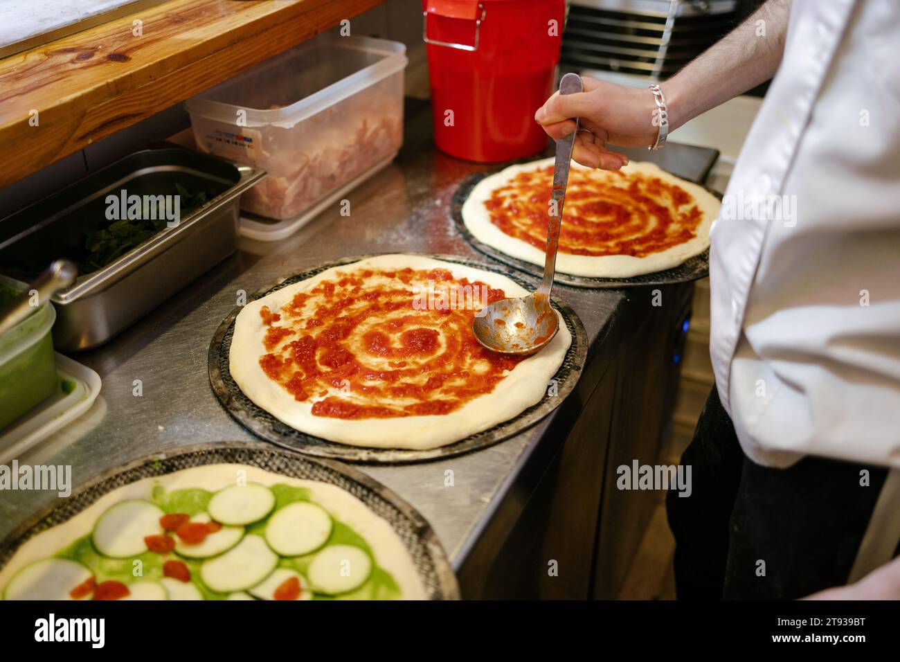 Detailaufnahme der Hände eines nicht erkennbaren Pizzabängers, der einer Pizza in einer Pizzeria Tomatensauce zufügt Stockfoto