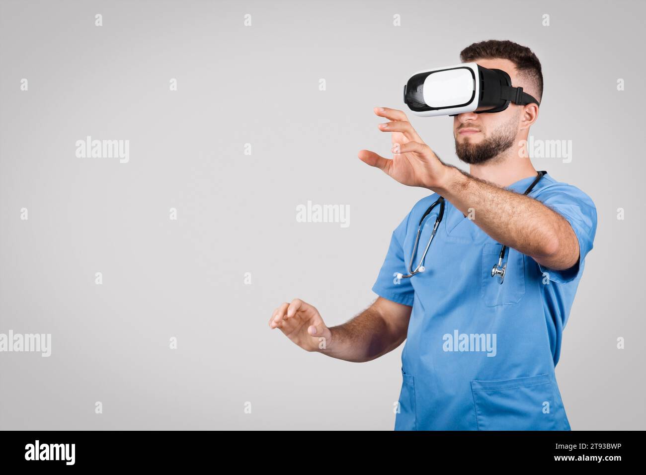 Männlicher Arzt in Blau mit VR-Brille Gesten, grauer Hintergrund, freier Platz Stockfoto