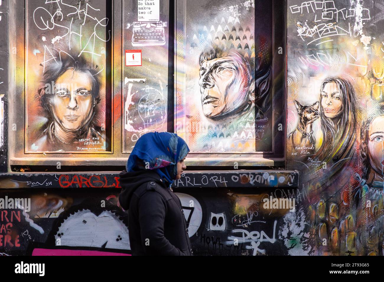 Eine Frau läuft an einer Wand vorbei, die mit hellen Graffiti und Street Art im East End-Viertel von London, Großbritannien, bedeckt ist Stockfoto