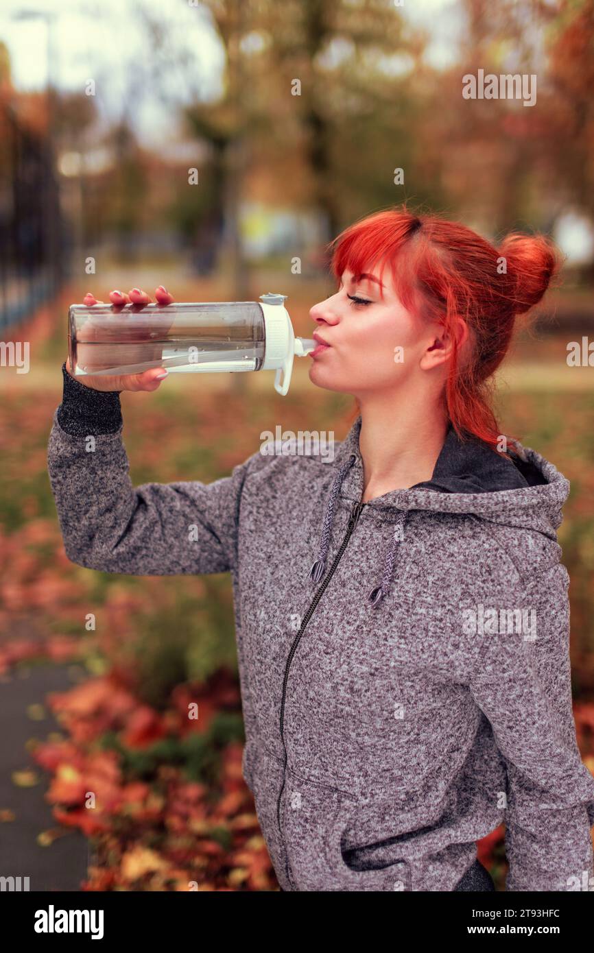 Readhead-Frau trinkt Wasser aus der Flasche im Park nach dem Training Stockfoto