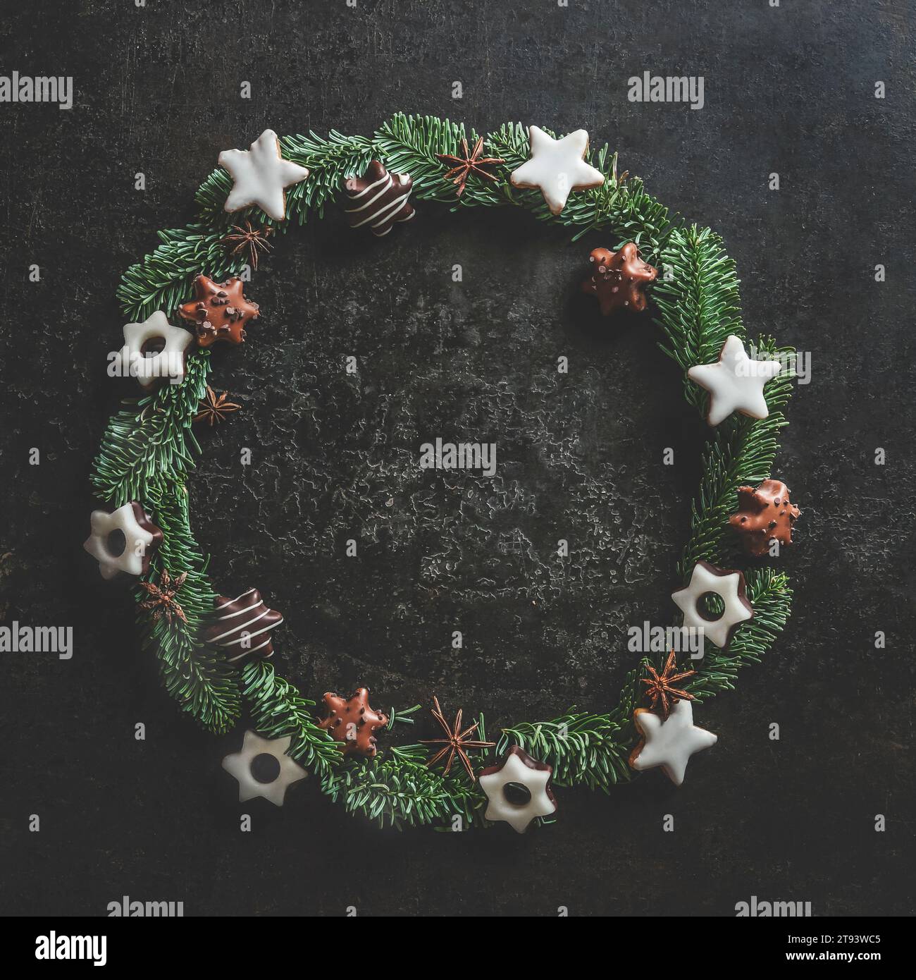 Weihnachtskreisrahmen mit Tannenkranz und Keksen auf dem Küchentisch aus dunklem Beton. Weihnachtlicher Hintergrund mit Kopierbereich. Draufsicht. Stockfoto