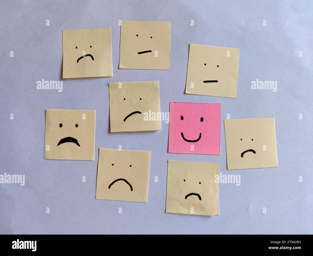 Das Konzept der positiven Einstellung. Handgezeichnet ein lächelndes Gesicht, das sich aus vielen traurigen Gesichtern abhebt, mit kleinen Büronotizen. Stockfoto