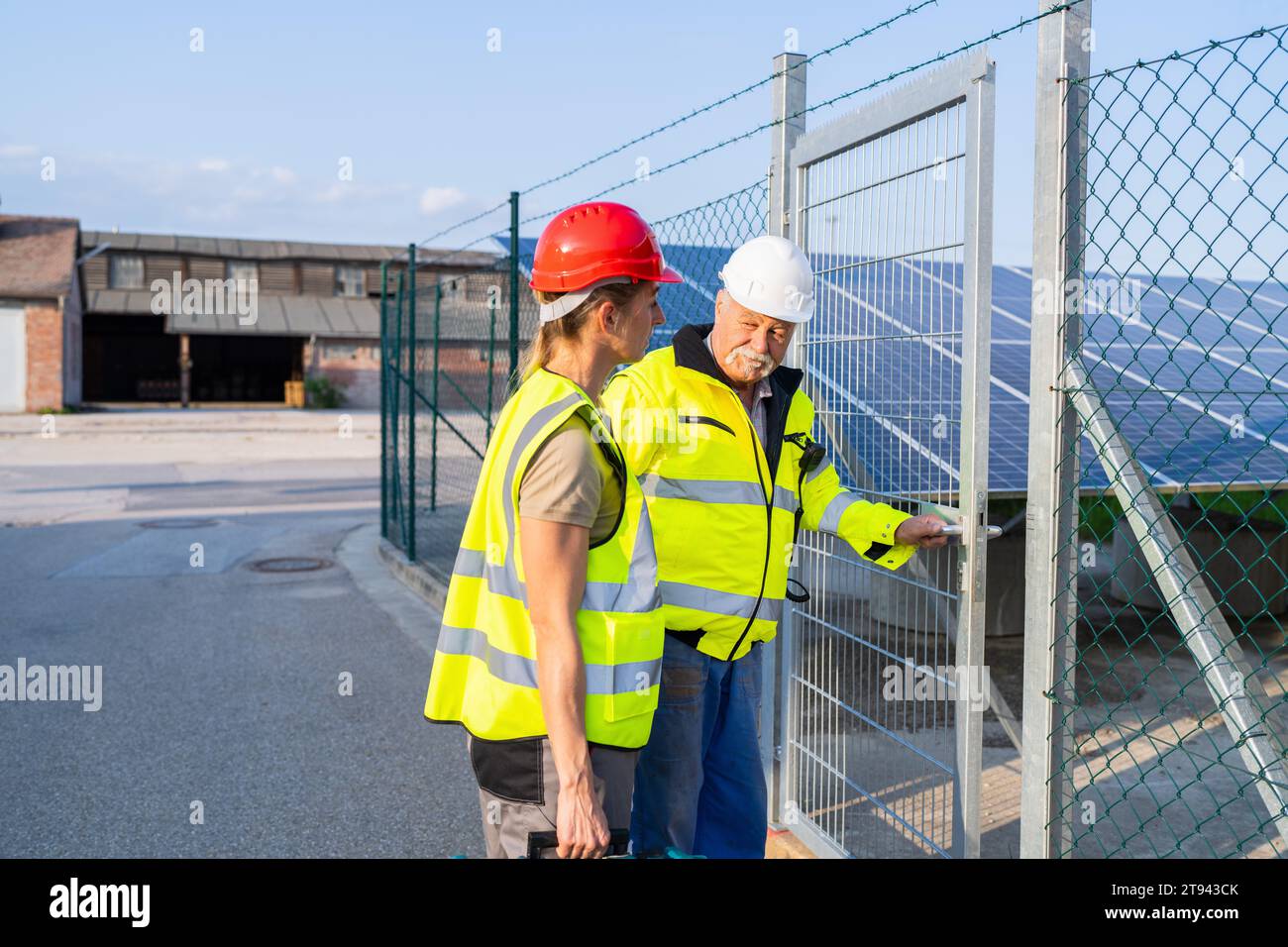 Zwei Ingenieure in gut sichtbaren Westen inspizieren ein Solarfeld, das an einem Tor der Anlage vorbeigeht Stockfoto