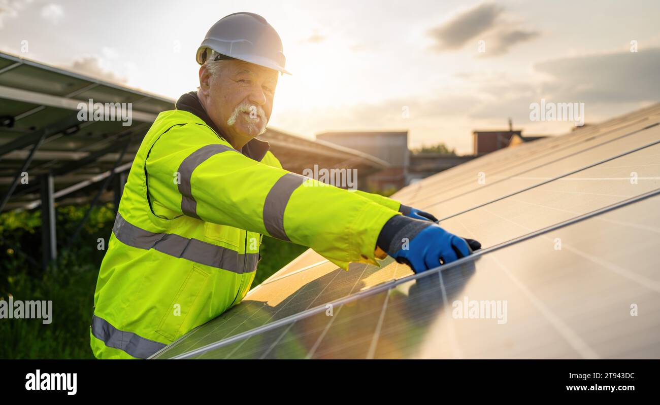 Leitender Ingenieur, der Sonnenkollektoren in einem Energiefarm bei Sonnenuntergang montiert. Alternatives energetisches ökologisches Konzeptbild. Stockfoto