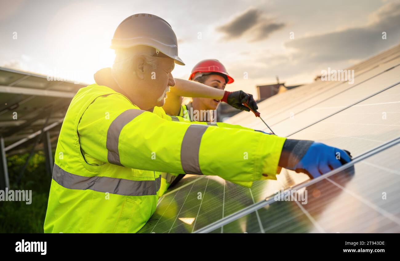 Team von Ingenieuren, die an der Wartung von Solarpaneelen bei Sonnenuntergang arbeiten. Alternatives energetisches ökologisches Konzeptbild. Stockfoto